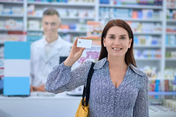 Улыбающаяся женщина показывает кредитку в аптеке — стоковое фото