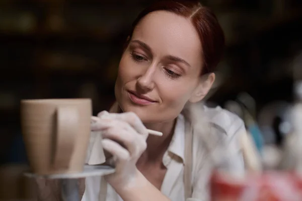 Uma jovem mulher pintando a cerâmica e olhando envolvido — Fotografia de Stock