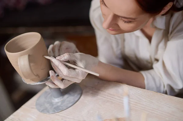 Uma jovem mulher pintando a cerâmica e olhando envolvido — Fotografia de Stock