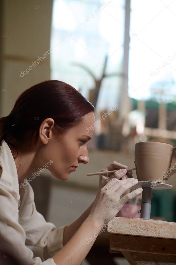 A young woman painting the cup and looking involved