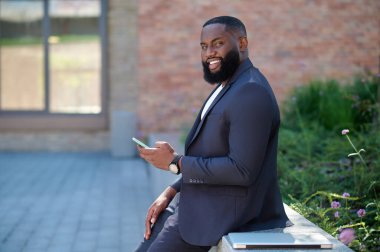 Elinde telefon olan takım elbiseli esmer bir adam.