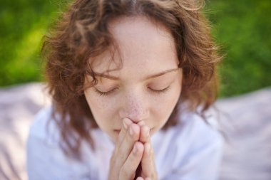 Genç bir kızıl parkta meditasyon yapıyor ve huzurlu görünüyor.