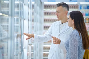 Beyaz önlüklü adam eczanedeki kadına danışmanlık yapıyor.