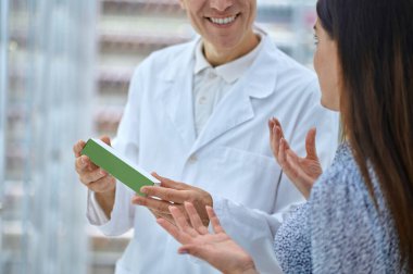 Tıbbi ürünlerle gülümseyen eczacı ve jest yapan kadın.