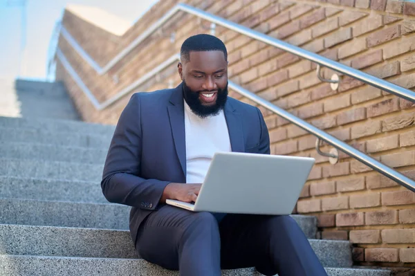 Egy kép egy sötét bőrű férfiről öltönyben egy laptoppal. — Stock Fotó