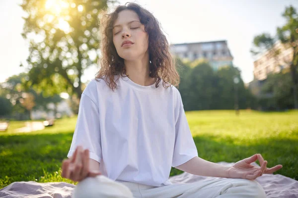 Dívka v bílém medituje v parku a vypadá pokojně — Stock fotografie