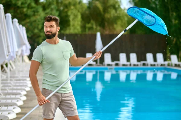 Темноволосый мужчина чистит бассейн и выглядит занятым. — стоковое фото