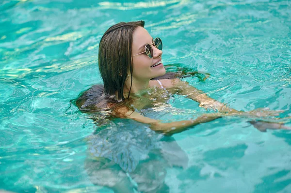 Μια χαριτωμένη γυναίκα με γυαλιά ηλίου που κολυμπάει στην πισίνα. — Φωτογραφία Αρχείου