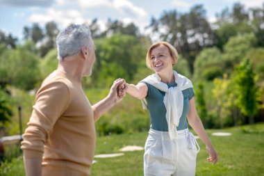 Dansçı, sarışın bir bayanın elini tutuyor.