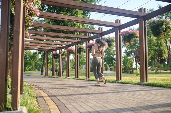 Parkta spor kıyafetleriyle koşan uzun saçlı bir kadın. — Stok fotoğraf