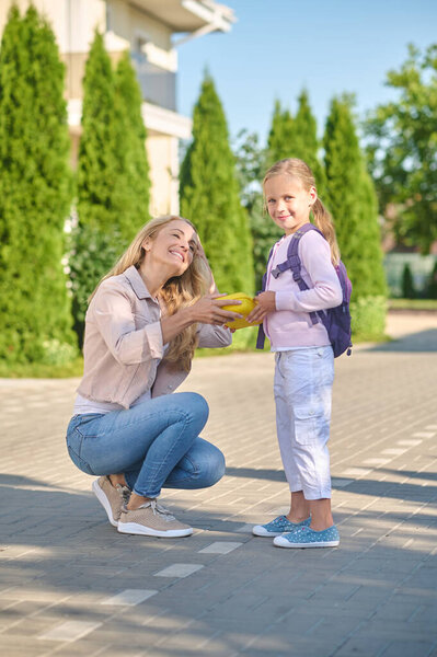 Joyful woman giving lunchbox to little girl