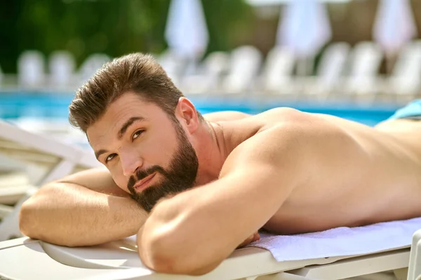 Um homem de cabelos escuros tomando banho de sol e olhando relaxado — Fotografia de Stock