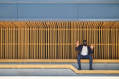VR gözlüklü koyu tenli bir adam bankta oturuyor.
