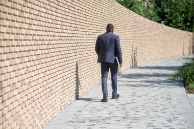 Koyu tenli bir adam tuğla duvarda yürüyor.