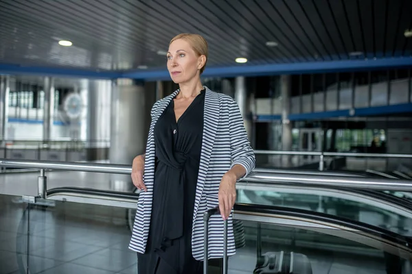 Серьезная стильная женщина с чемоданом в терминале аэропорта — стоковое фото