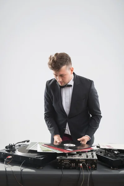 DJ in tuxedo looking at his vinyl records standing by turntable — Stock Photo, Image