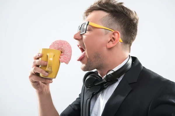 Dj guapo hipster comer donut de su taza en el lugar de trabajo —  Fotos de Stock