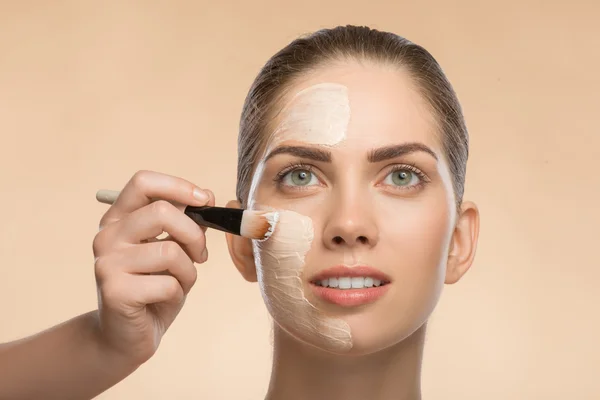 Menina bonita no spa aplicando creme cosmético facial com escova — Fotografia de Stock