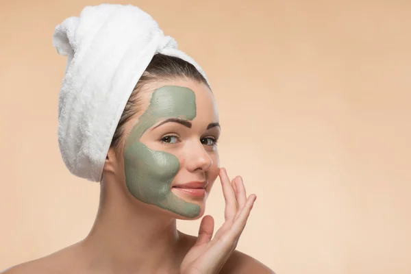 Spa girl with a  towel on her head applying facial clay mask and — Stock Photo, Image