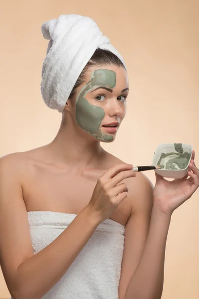 Spa girl with a  towel on her head applying facial clay mask and — Stock Photo, Image