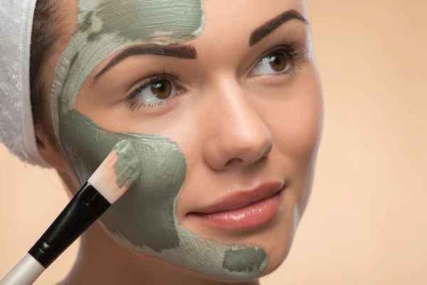 Spa girl with a  towel on her head applying facial clay mask and — Stock Photo, Image