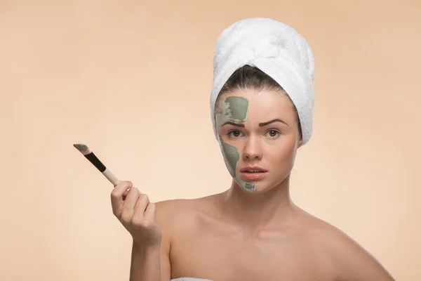 Spa chica con una toalla en la cabeza la aplicación de la máscara de arcilla facial y — Foto de Stock