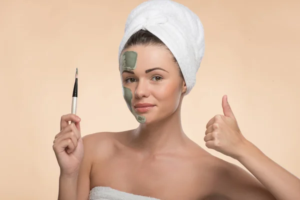 Spa girl with a  towel on her head applying facial clay mask and — Stock Photo, Image