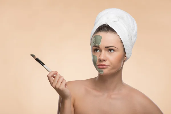 Spa girl with a  towel on her head applying facial clay mask and — Stock Photo, Image