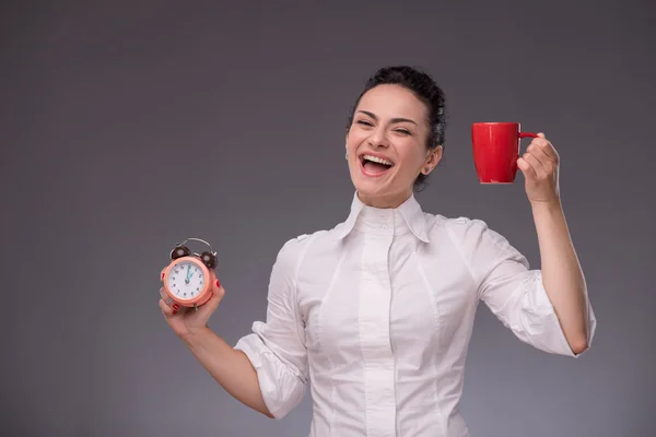 Menina feliz segurando um despertador e um copo vermelho — Fotografia de Stock