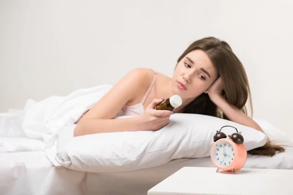 Belleza acostada en la cama con un reloj y pastillas — Foto de Stock