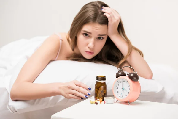 Belleza acostada en la cama con un reloj y pastillas — Foto de Stock