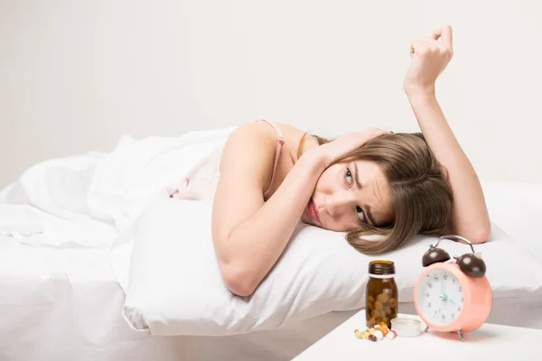 Belleza acostada en la cama con un reloj y pastillas — Foto de Stock