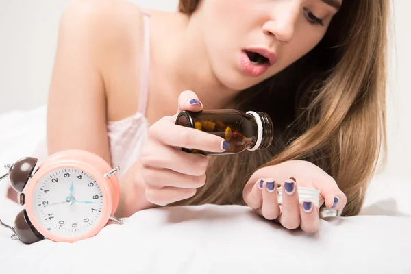Belleza acostada en la cama con un reloj y pastillas — Foto de Stock