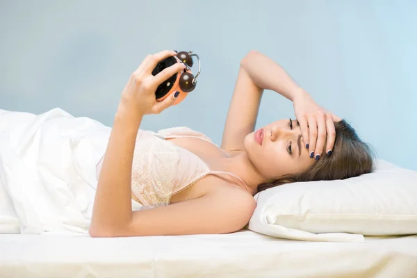 Beauty lying on the bed with a clock — Stock Photo, Image