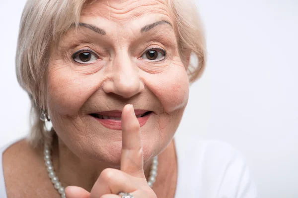 Пожилая женщина кладет палец на рот — стоковое фото