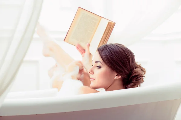Красивая молодая женщина в ванной с книгой — стоковое фото