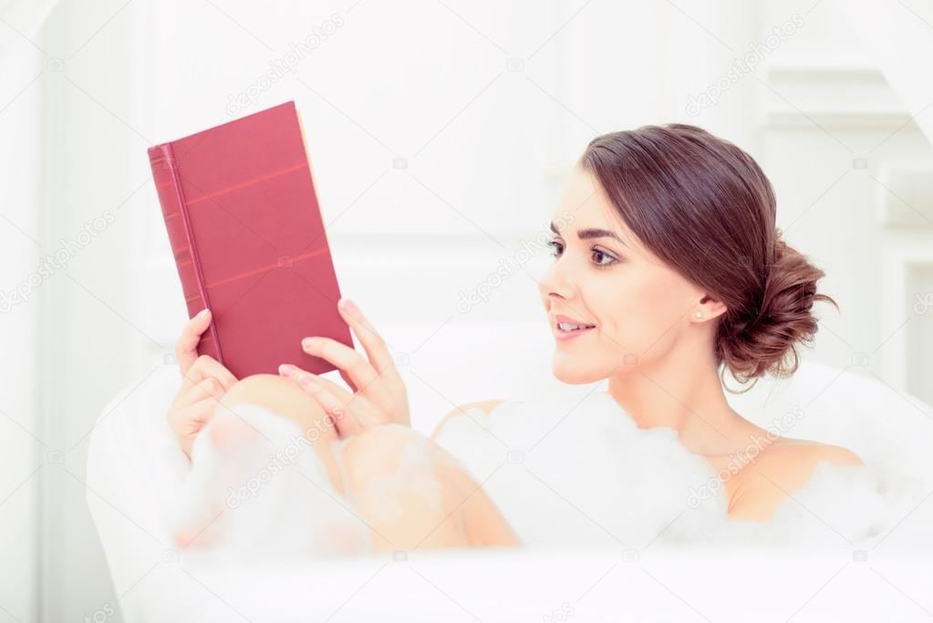 Beautiful young woman in bath with a book