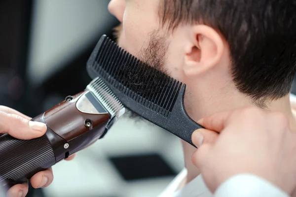 El hombre se afeita la barba con un cortador de pelo —  Fotos de Stock