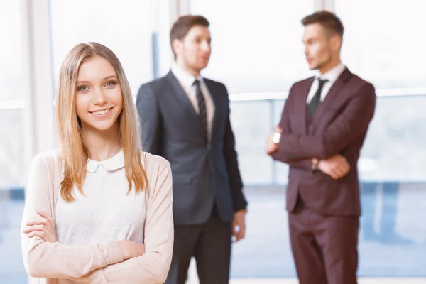 Blond young business woman standing in front of two men talking — Stock Photo, Image