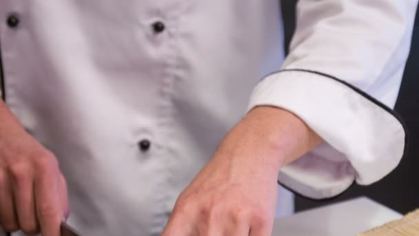 Vertical dolly shot of smiling Asian chef cutting appetizing sushi rolls — Stock Video