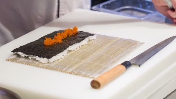 Asian chef in white uniform putting caviar on sushi rolls — Stock Video