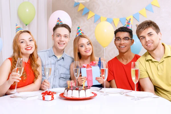 Jóvenes celebrando un cumpleaños sentados a la mesa —  Fotos de Stock