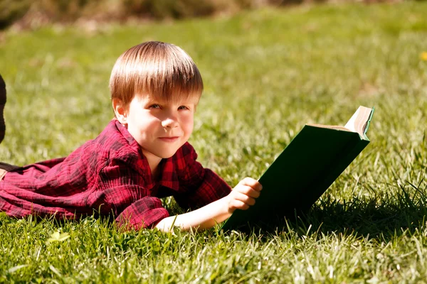 Küçük çocuk kitabı ile çim üzerinde yalan gülümseyen — Stok fotoğraf