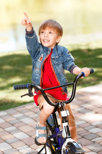 Petit garçon souriant à vélo et pointant vers le haut — Photo