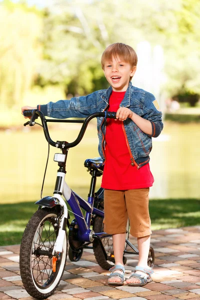 Petit garçon souriant debout à côté du vélo — Photo