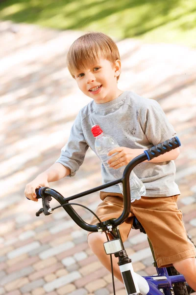 Garçon souriant vélo d'équitation avec bouteille d'eau — Photo