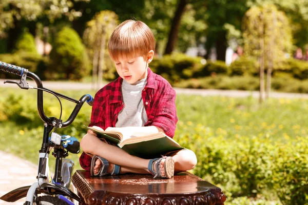 Niño sentado en el banco y leyendo libro. — Foto de Stock