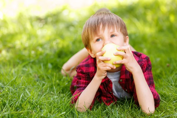 Kleine jongen liggen op gras met apple — Stockfoto