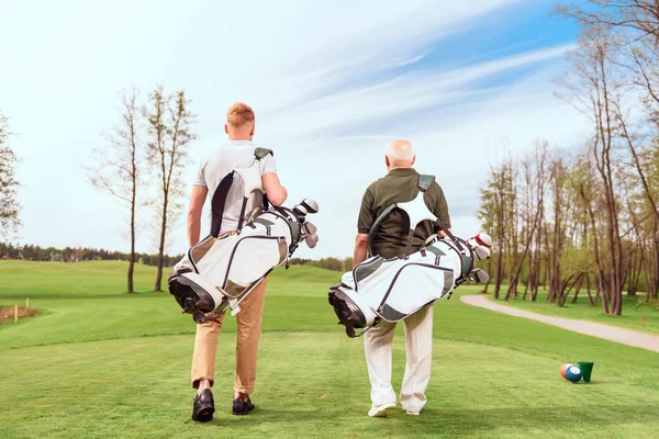 Vista trasera de los jugadores de golf caminando en el campo —  Fotos de Stock