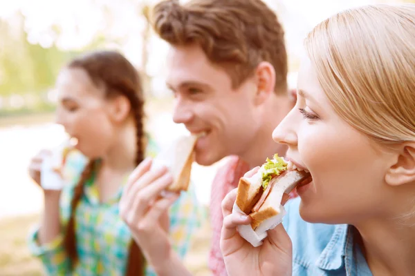 Young people eating sandwiches during picnic — Stock Photo, Image